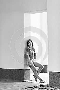 Black and white full length portrait of beautiful happy brunette young woman in casual style standing and leaning on wall, posing