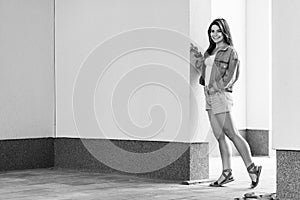 Black and white full length portrait of beautiful happy brunette young woman in casual style standing and leaning on wall, posing