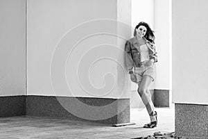 Black and white full length portrait of beautiful happy brunette young woman in casual style standing and leaning on wall, posing