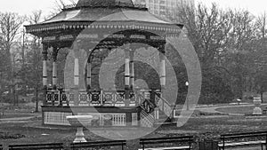 Black and white gazebo in public gardens during snow flurries.