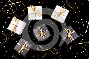 Black and white gift boxes with gold ribbon on shine background. Flat lay.