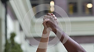 Black and white hands clenched together in a fist in protest against the backdrop of a city street. A political