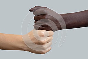 Black and white hands in the shape of fists, placed on top of each other. Grey  background. The concept of inter-racial