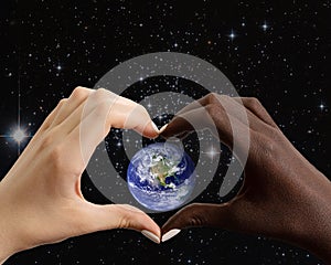 Black and white hands in the shape of a heart with the planet Earth on a background of the starry sky