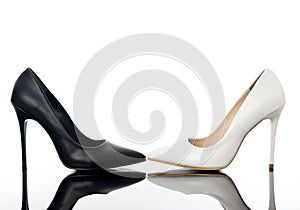 Black and white high heels pointed woman stiletto shoes on reflective floor.