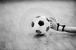 Black and white image of ball in hands of futsal goalkeeper on wooden futsal floor