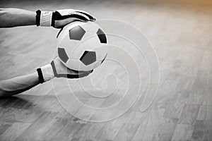 Black and white image of ball in hands of futsal goalkeeper on wooden futsal floor