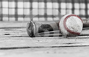 Black and white image of a baseball and bat on wood surface.