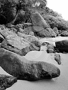 Black and white image of big rocks and cliffs on the beach of ocean lagoon at tropical island