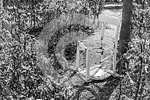 Black white image of a broken white chair in a garden Labyrinth, Germany
