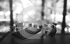 Black and white image of a calculator , piggy bank , coins stack and a glass money jar on the table