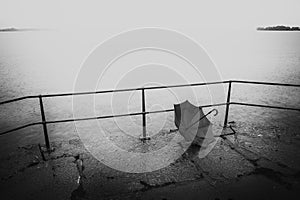 Black and white image of forgotten umbrella a rainy day by the water