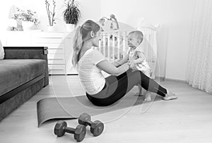Black and white image of happy mother exercising on floor with h