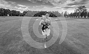 Black and white image of happy mother running on grass at park w