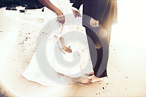 Black and white image of lower half of bride and groom standing barefoot on the sand