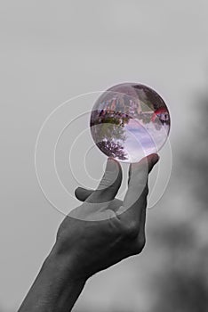 Black and white image of man balancing purple glass sphere on the end of his finger and thumb