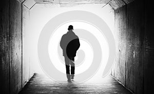 black and white image of a man hands in pockets walking away in a dark tunnel towards the light. photo