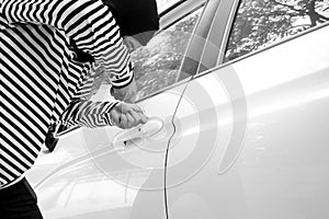 Black and white image of the man robber with a balaclava on his head trying to break into the car/Criminal and car