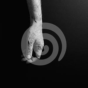 Black & white image of man`s hand hanging loosely, isolated against a black background with dramatic sidelight