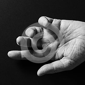 Black & white image of man`s hand, open palm up and pointing, isolated against a black background with dramatic sidelight