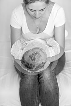 Black and white image of mother sitting on bed and holding her b