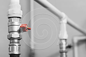 Black and white image of plumbing valve with red faucet on the plastic water pipe of plumbing system. Close-up