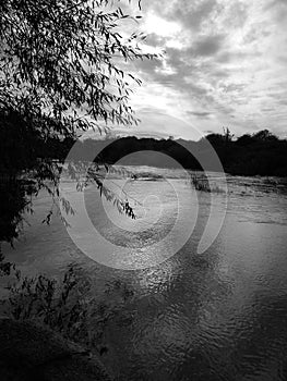 Black and white image of the river at twilight with cloudy sky