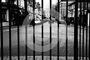 Black and white image of a road through black metal gate