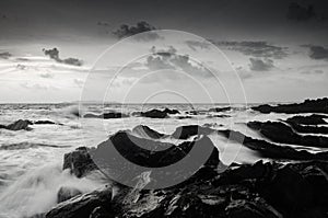 Black and white image of seashore and wave hitting rock on the b