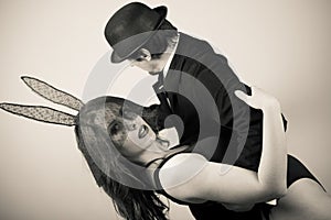 Black and white image of beautiful young lady wearing bunny ears dancing with man in hat on light background