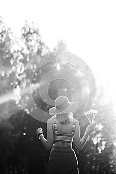 Black and white image. Silhouette of girl walking in park outdoor. Sunny summer lifestyle concept. Woman in dress and hat in field