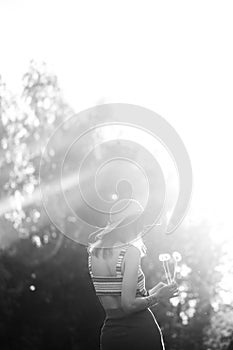 Black and white image. Silhouette of girl walking in park outdoor. Sunny summer lifestyle concept. Woman in dress and hat in field