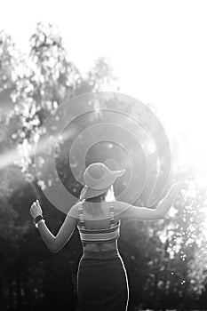 Black and white image. Silhouette of girl walking in park outdoor. Sunny summer lifestyle concept. Woman in dress and hat in field