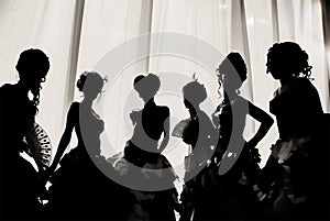Black and white image of the silhouette of girls and women in carnival costumes and ball dresses in the theater on the stage behin