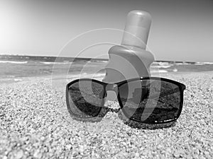 Black and white image of sunglasses and sun protection creme lying on the sandy beach at sea. Perfect image for