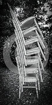 Black and white image of vertical stacked chairs outdoors.