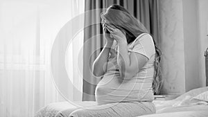 Black and white image of young pregnant woman suffering from depression crying on bed. Concept of maternal and pregnancy
