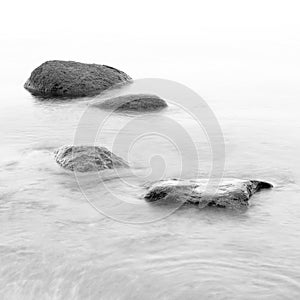 Black and white impression of the evening sea shore with water and stones on a beach