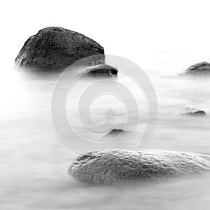 Black and white impression of the evening sea shore with water and stones on a beach