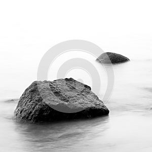 Black and white impression of the evening sea shore with water and stones on a beach