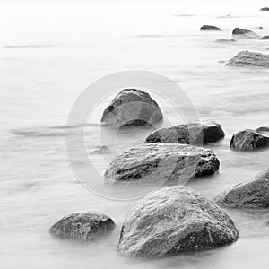 Black and white impression of the evening sea shore with water and stones on a beach