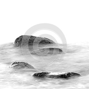 Black and white impression of the evening sea shore with water and stones on a beach