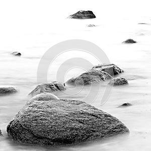 Black and white impression of the evening sea shore with water and stones on a beach