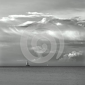 Black and white impression of a lonely sailboat sailing on a sea under mosaic of clouds