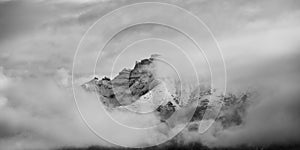 Black and white landscape of mountain top covered by snow and clouds