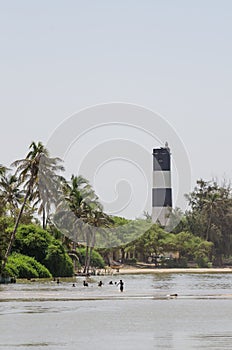 Black and white lighthouse with palms, trees and swimming locals at the sea, Ndiebene, Senegal photo