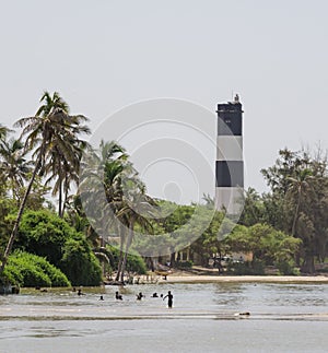 Black and white lighthouse with palms, trees and swimming locals at the sea, Ndiebene, Senegal photo