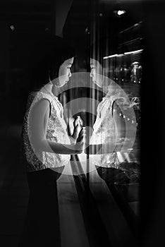 The black and white low key image of the young girl staring at the showcase, which is like a mirror, reflecting her as another.