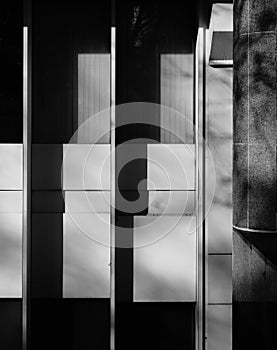 Black and white monochrome image of facade of 1980s office building with graded high contrast shadowing cast over the windows on