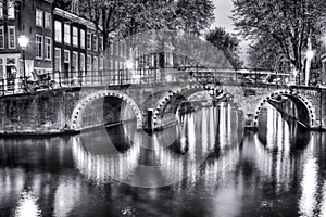 Black and White Night View of Amterdam Cityscape with One of Its Canals. With Illuminated Bridge and Traditional Dutch Houses